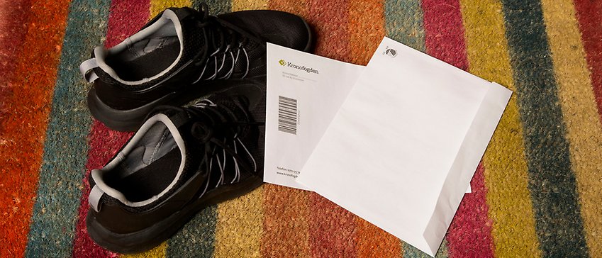 Svarta sneakers och två kuvert på färgglad randig dörrmatta