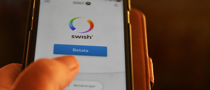 Tumme klickar på betala-knappen i appen Swish på en mobil
